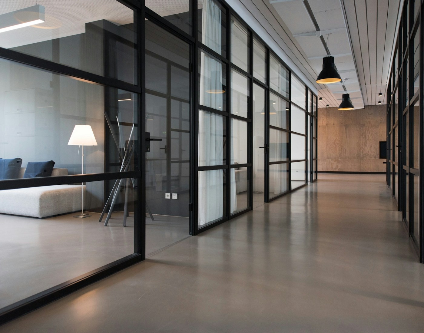 A quiet office corridor framed by glass meeting rooms and warm wood